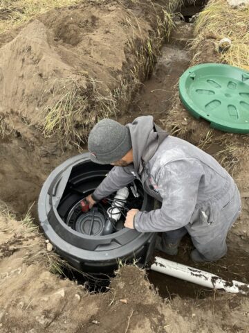Plumber working on septic tank pump installation – Flathead Valley drain field repair service.”